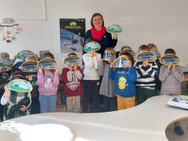 Lisa Milana stands at the center of a classroom of students holding up GPM water cycle handouts. 