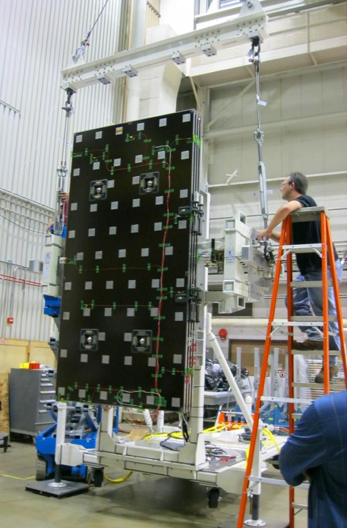 Engineers on a ladder inspecting the solar panel as it sits vertically.